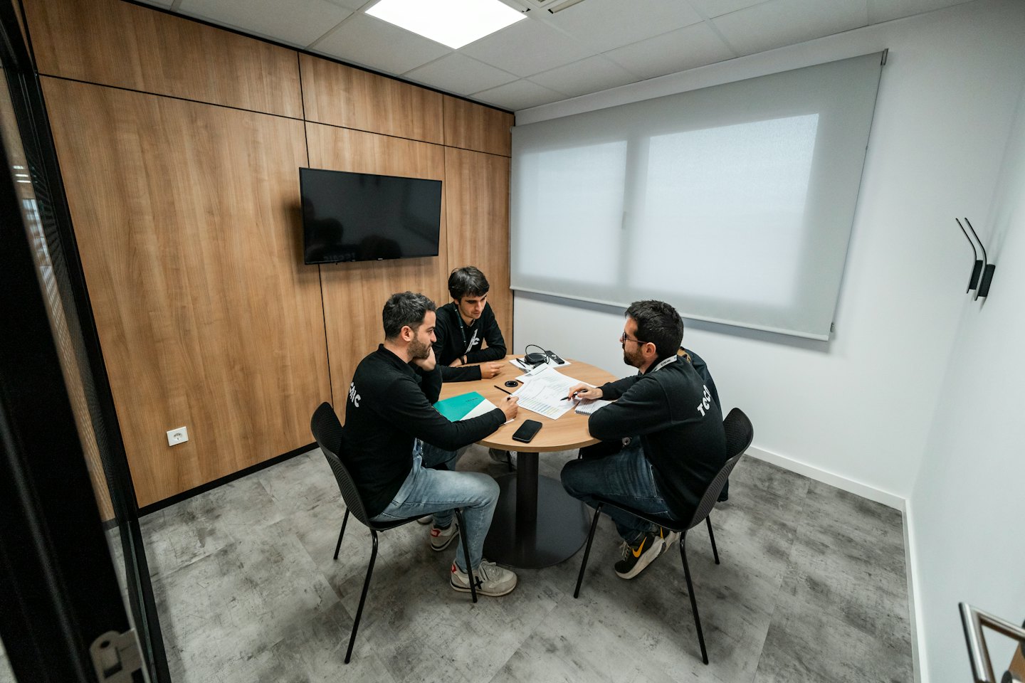 Tre professionisti discutono documenti a un piccolo tavolo da riunione.