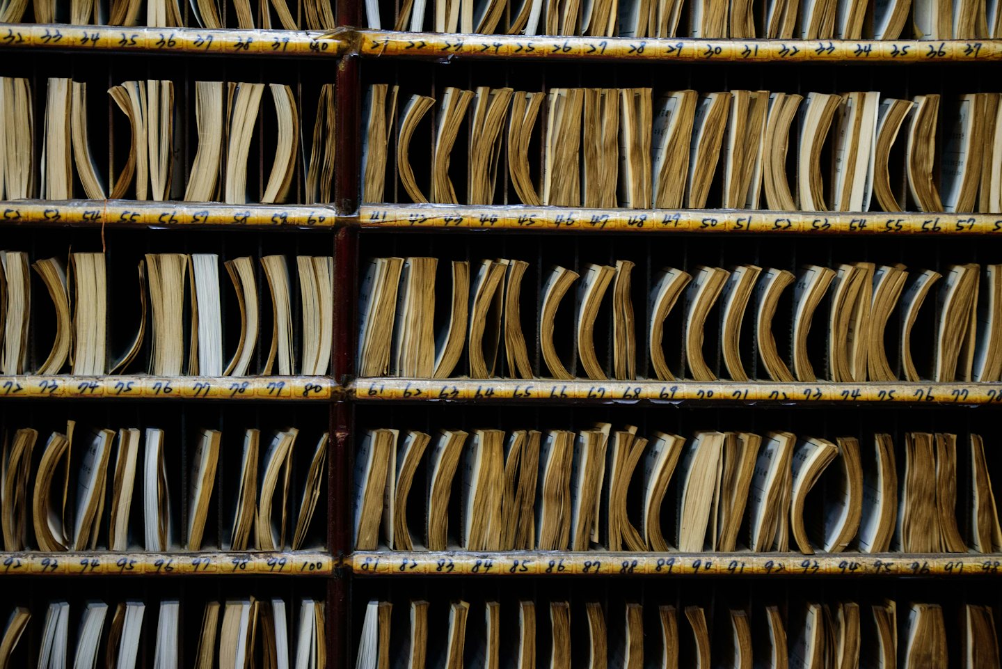 File di schedari in legno contengono documenti d'archivio ordinatamente impilati.