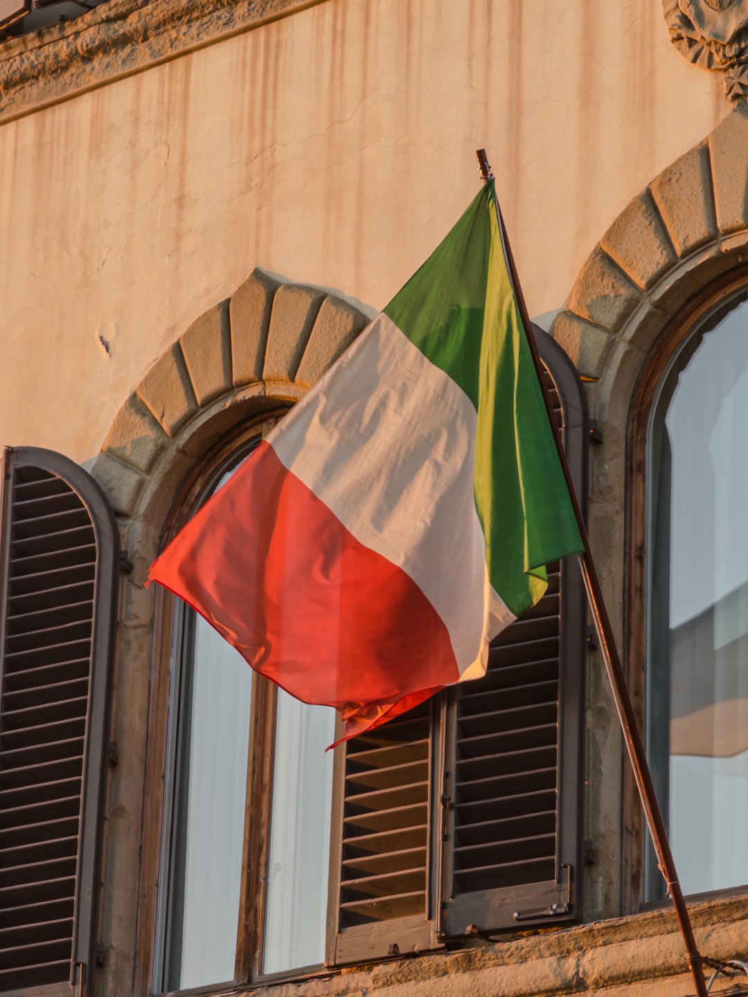 Facciata di un edificio storico in pietra con bandiera italiana che sventola.