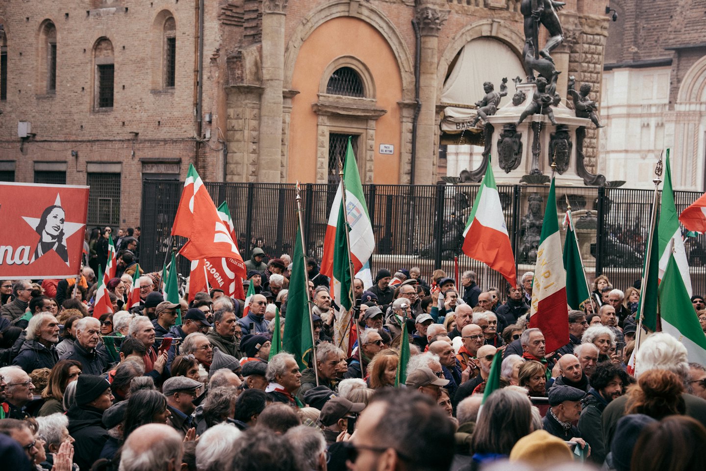 Una folla di persone sventola bandiere italiane in una piazza cittadina.